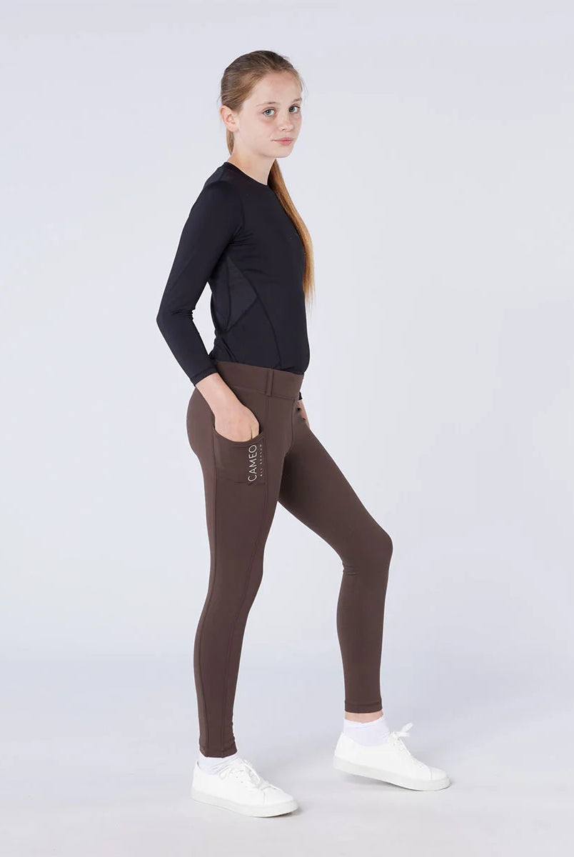 CAMEO All Season Riding Tights in Chocolate Brown worn by a junior rider, featuring a deep ergonomic thigh smartphone pocket with CAMEO branding. These technical equestrian leggings provide thermal brushed lining, 4-way compression stretch, and a full-seat silicone grip for all-weather riding in the UK.