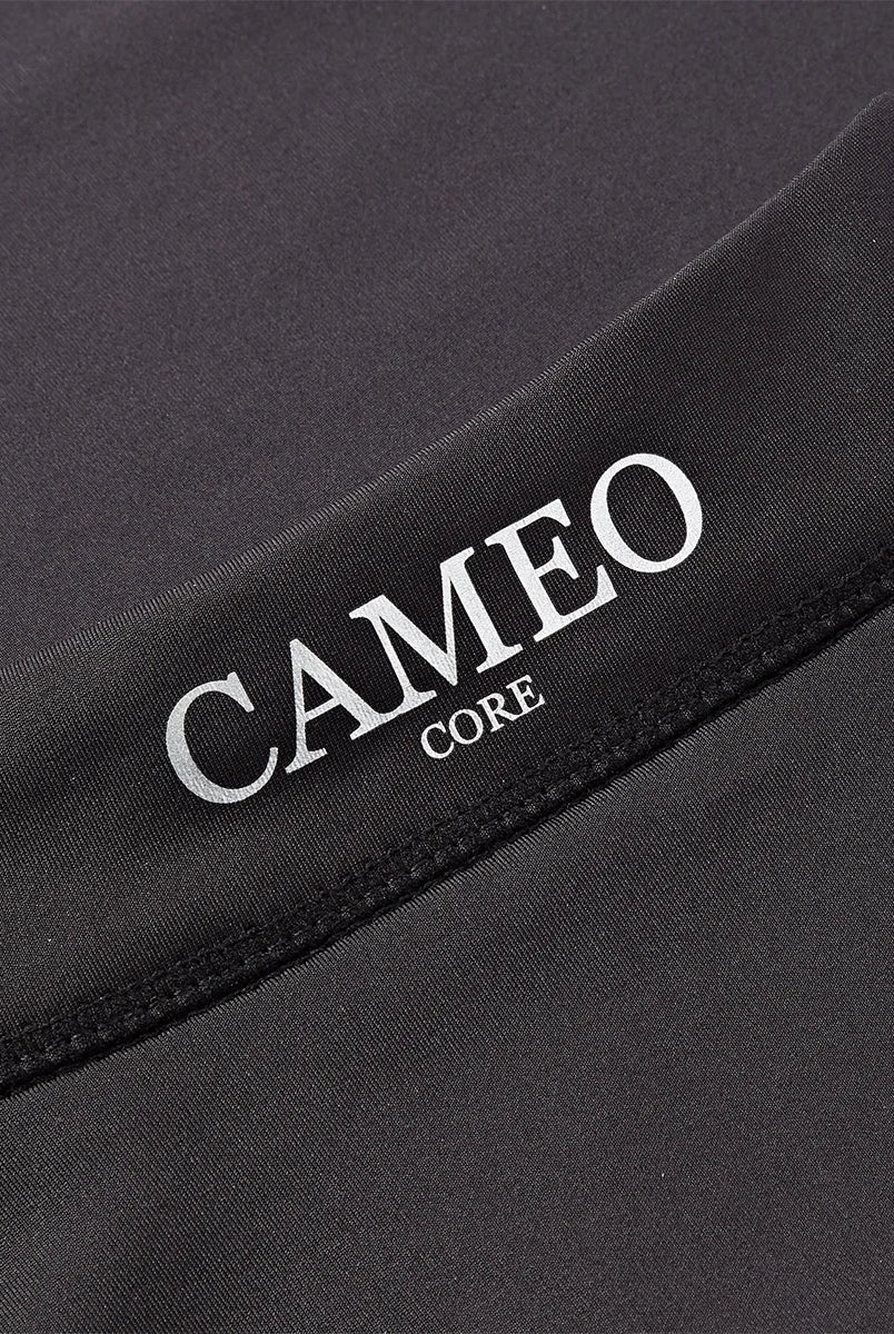 CAMEO Core Collection Baselayer in Black featuring a macro view of the reflective silver CAMEO CORE branding and premium anti-chafing flat-lock seams. The technical 4-way stretch CameoTech microfibre fabric is visible, engineered for active thermoregulation and professional equestrian performance.
