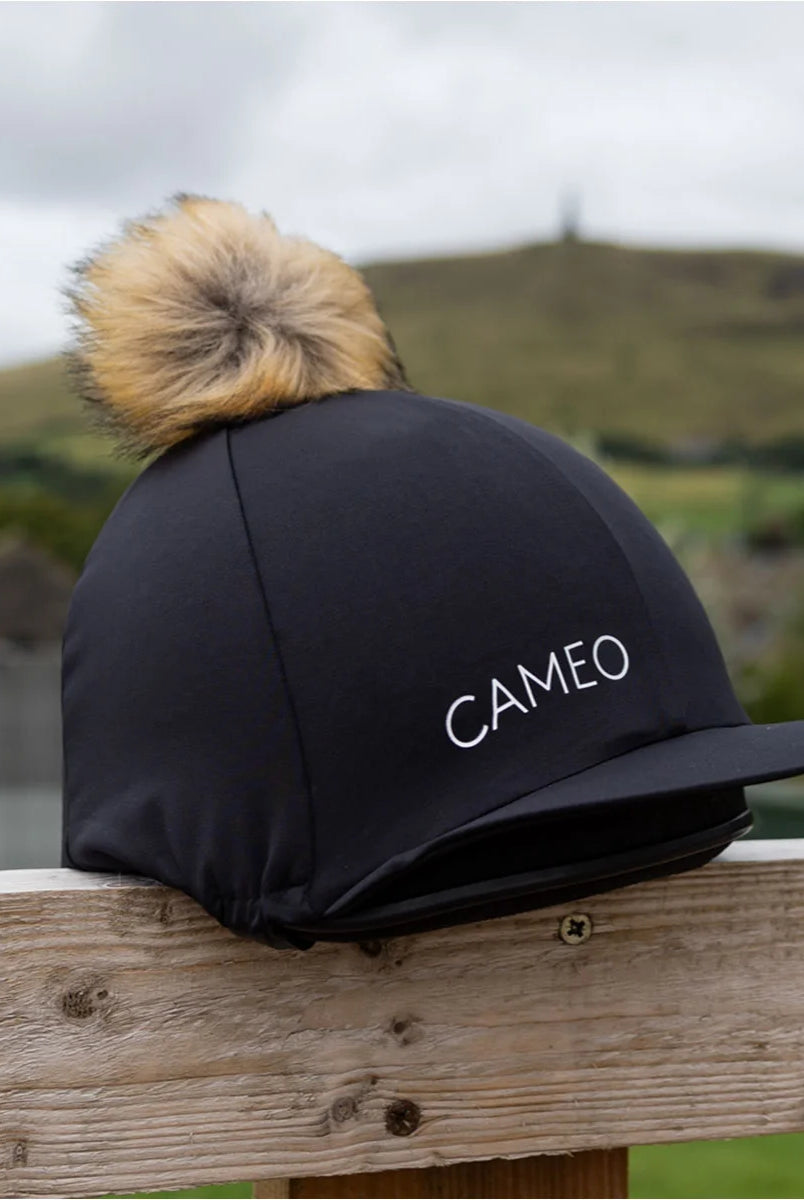 CAMEO Core Hat Silk in Black featuring a luxurious honey-toned faux-fur pom-pom and 4-way stretch technical fabric for a wrinkle-free fit. This premium equestrian helmet cover is designed in the UK with a flexible peak and secure elasticated hem, perfect for matching with the CAMEO CORE collection.