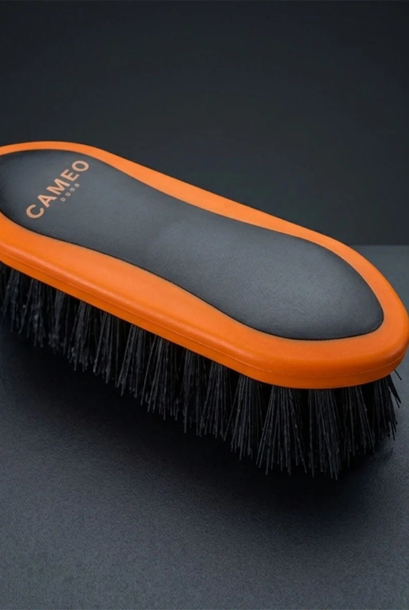 CAMEO Dandy Brush in Orange on a studio background featuring stiff, long bristles to flick away dried mud and loose hair.