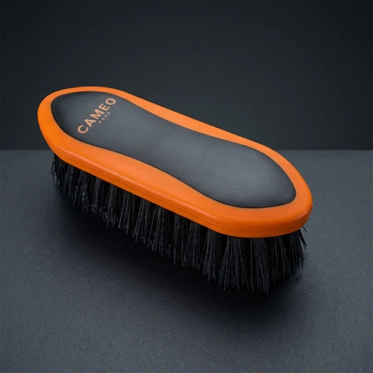 CAMEO Dandy Brush in Orange on a studio background featuring stiff, long bristles to flick away dried mud and loose hair.