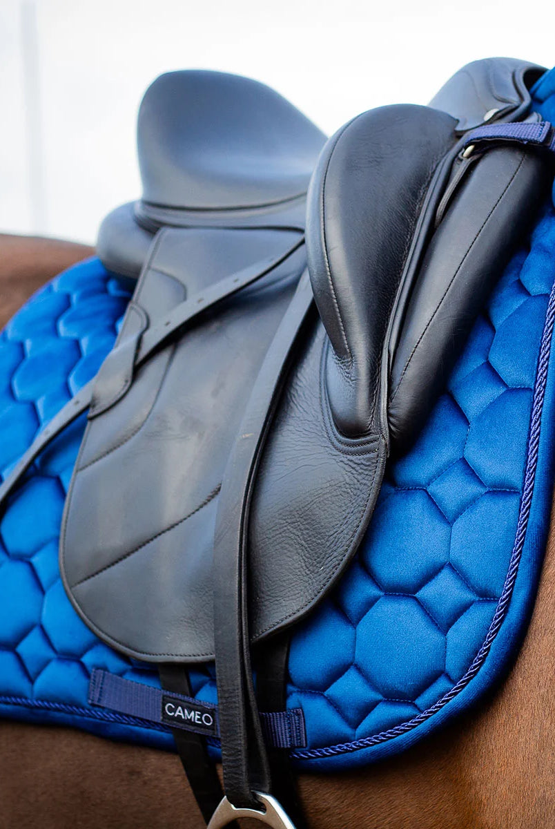 CAMEO Suede Dressage Saddlecloth in Navy viewed in an angled close-up beneath a dressage saddle on a horse, highlighting the straight flap cut, honeycomb quilting, rope piping, and reinforced girth loop engineered for shock absorption and non-slip stability during intensive dressage schooling.