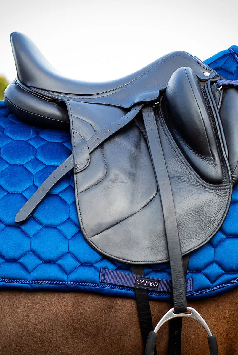 CAMEO Suede Dressage Saddlecloth in Navy fitted beneath a black leather dressage saddle on a bay horse, showcasing the straight-cut square profile, hexagonal honeycomb quilting, rope piping, and branded girth protection panel engineered for shock absorption, spinal relief, and arena performance.