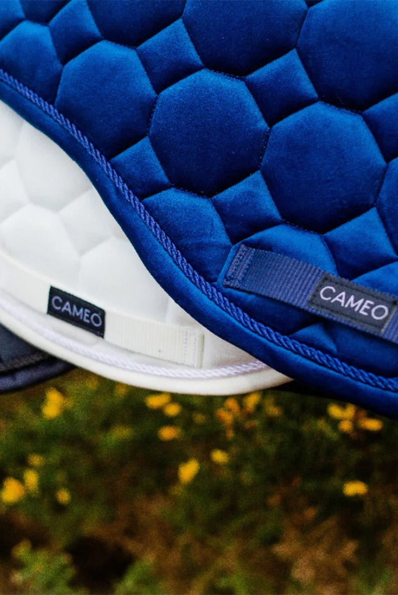 CAMEO Suede GP & Jump Saddlecloth in Navy in a macro detail shot stacked over White and Black pads, showcasing the reinforced girth protection panel with woven logo badge, rope piping, and geometric quilting engineered for anti-wear durability and saddle security.
