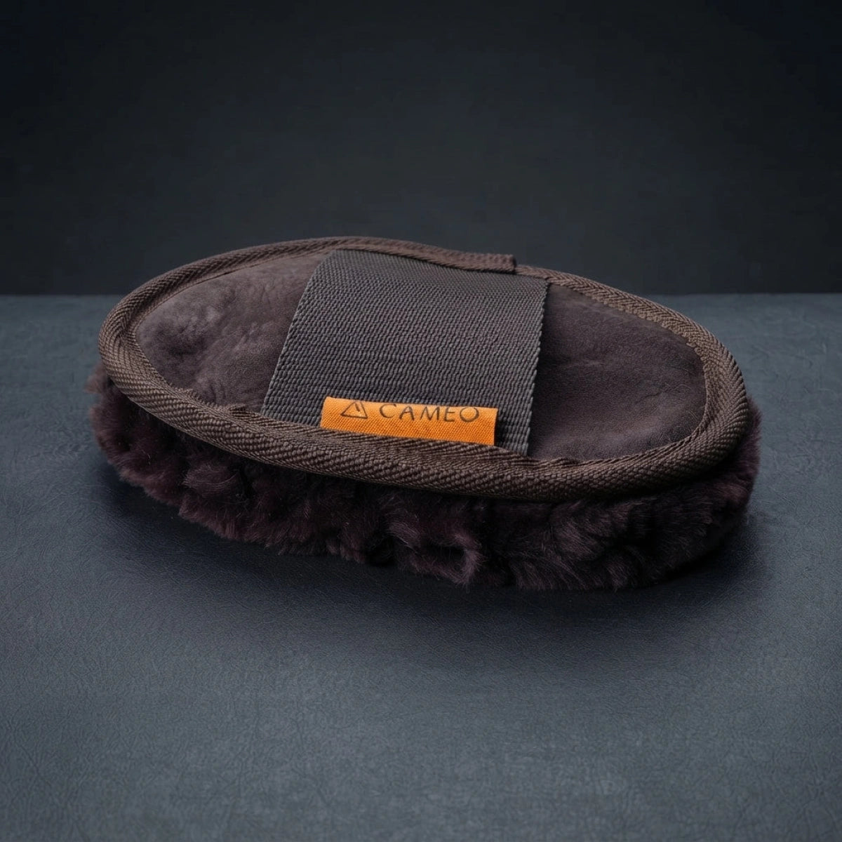 A dark brown faux-fur slouchy shoe cover with a dark brown canvas strap and an orange brand label reading '25 CAMEO', set against a dark gray background.