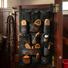 A black equestrian shoe brush organizer hanging on a dark wooden door, holding multiple horse grooming tools including brushes, hoof files, and a leather bridle.