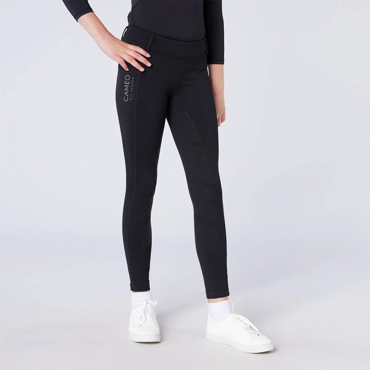 CAMEO All Season Riding Tights in Black featuring a deep thigh smartphone pocket and innovative full-seat chevron silicone grip. Worn by a junior rider, these technical equestrian leggings include a high-rise core-supporting waistband and thermal brushed lining for all-weather training in the UK.