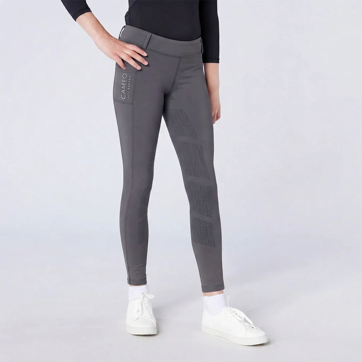 CAMEO All Season Riding Tights in Dark Grey featuring a deep thigh smartphone pocket and innovative full-seat chevron silicone grip. Worn by a junior rider, these technical equestrian leggings include a high-rise core-supporting waistband and thermal brushed lining for all-weather training in the UK.