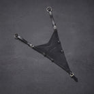 A black leather bib martingale with adjustable straps, metal buckles, and two circular D-rings, laid flat on a dark grey textured surface with CAMEO embossed on the leather