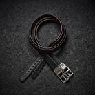 A dark brown leather wrapped stirrup leather with a silver-tone metal buckle, neatly coiled on a dark textured background.