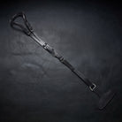 A black leather horse crupper with crupper T strap laid diagonally on a dark textured leather surface, featuring silver-toned metal buckles and a padded black handle.
