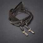A dark brown leather side rein strap with silver metal buckles and clips, coiled on a dark gray textured background.