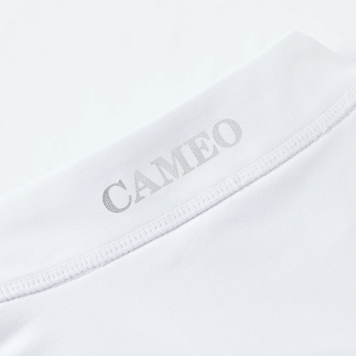 CAMEO Core Collection Baselayer in White showcasing a macro view of the reflective silver CAMEO logo and premium anti-chafing flat-lock seams. This technical detail highlights the breathable CameoTech 4-way stretch fabric engineered for professional equestrian competition and training comfort.