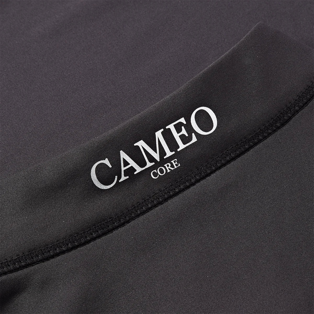 CAMEO Core Collection Baselayer in Black featuring a macro view of the reflective silver CAMEO CORE branding and premium anti-chafing flat-lock seams. The technical 4-way stretch CameoTech microfibre fabric is visible, engineered for active thermoregulation and professional equestrian performance.