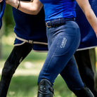 CAMEO Core Woven Stretch Belt in Navy worn with riding tights and tall boots, showcasing the holeless braided elastic weave, leather chapes, and polished stirrup buckle engineered for flexible rider comfort and waistband security in the saddle.
