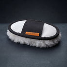 A Natural lambswool mitt with a natural elastic strap featuring the orange 'CAMEO' brand logo, displayed on a dark gray textured surface. for polishing horses coats before competition.