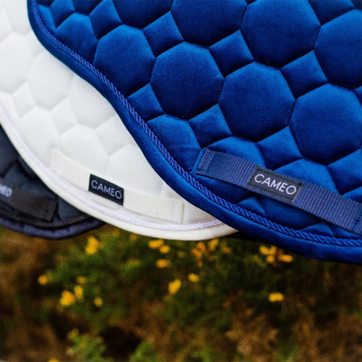 CAMEO Suede GP & Jump Saddlecloth in Navy in a macro detail shot stacked over White and Black pads, showcasing the reinforced girth protection panel with woven logo badge, rope piping, and geometric quilting engineered for anti-wear durability and saddle security.