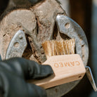 CAMEO The Hoof Hero Elite Edition in Natural Wood in use scrubbing dirt and grit from around a shod horse hoof frog.