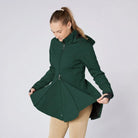 CAMEO Zenith Pro Ride Coat in EverGreen demonstrated by a model holding open the flared riding skirt, showcasing the two-way front zip, thermal fleece lining, and expansive saddle coverage engineered for unrestricted seat and leg aids in wet weather.