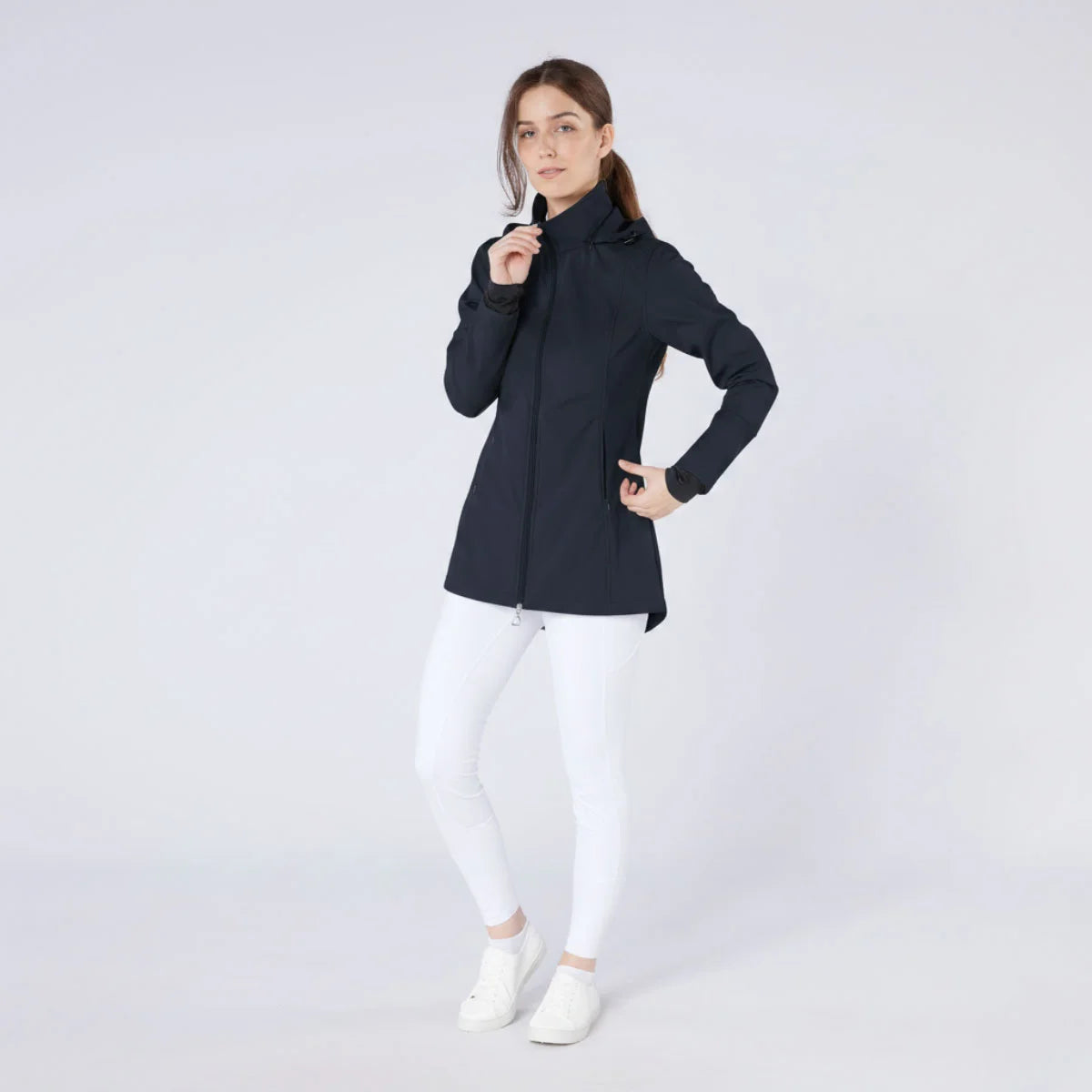CAMEO Zenith Pro Ride Coat in Navy modelled on a studio model in white riding tights, showcasing the tailored longline waterproof cut, high storm collar, two-way stirrup zip, and thumb-loop cuffs engineered for cold-weather riding and yard duty comfort.