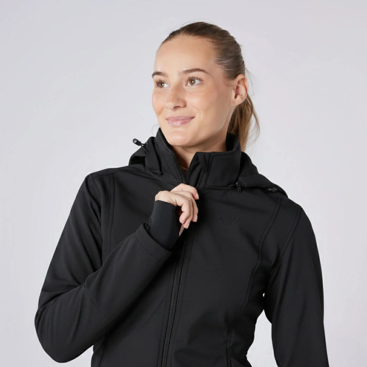 CAMEO Zenith Pro Ride Coat in Black modelled on a female equestrian, showcasing the high fleece-lined storm collar, stretch thumb-loop cuffs, detachable hood, and tonal logo engineered for windproof warmth and foul-weather riding comfort.