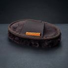 A brown lambswool mitt with a brown elastic strap featuring the orange 'CAMEO' brand logo, displayed on a dark gray textured surface. for polishing horses coats before competition.